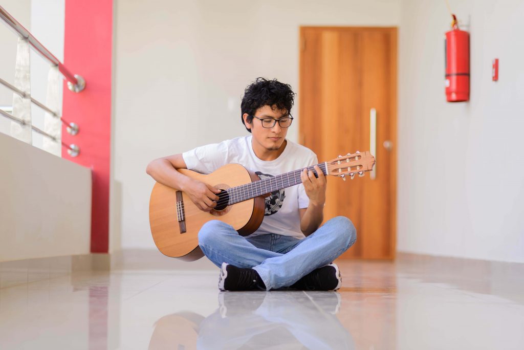 Foto de estudiante tocando guitarra en pasadizo de la universidad.