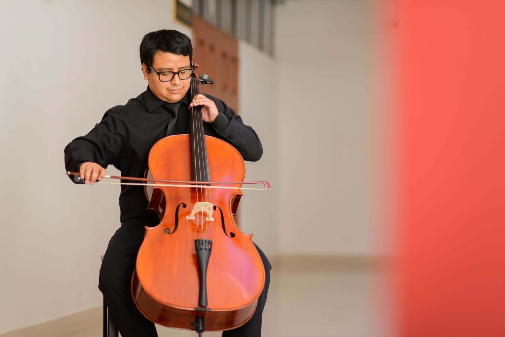 Foto (en plano americano) de estudiante interpretando pieza musical con chelo.